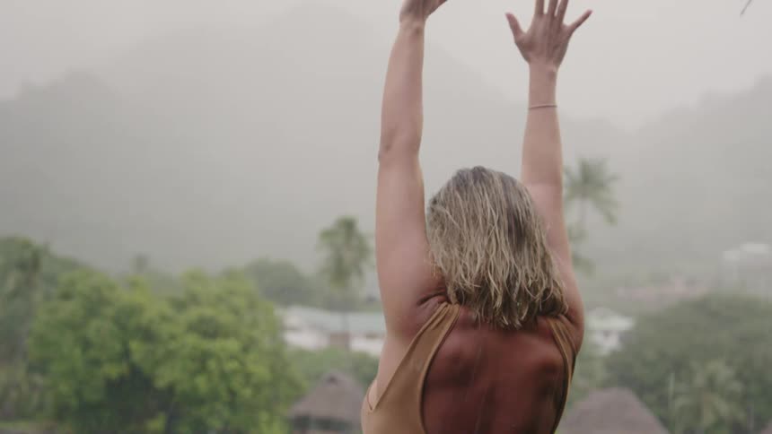 A woman in front of a lagoon putting her hands up in the rain