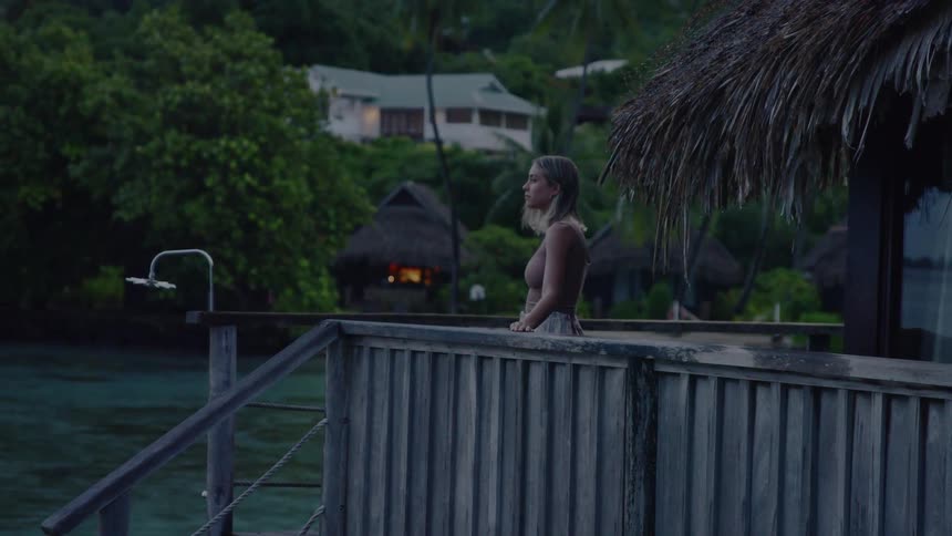 A woman walks on a deck with wooden railing overlooking the water
