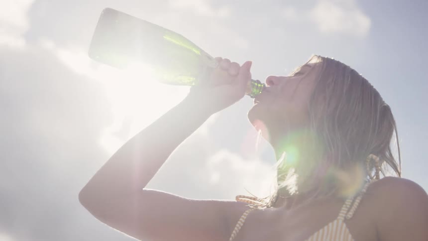 Woman drinking white wine from the bottle against the sunlight