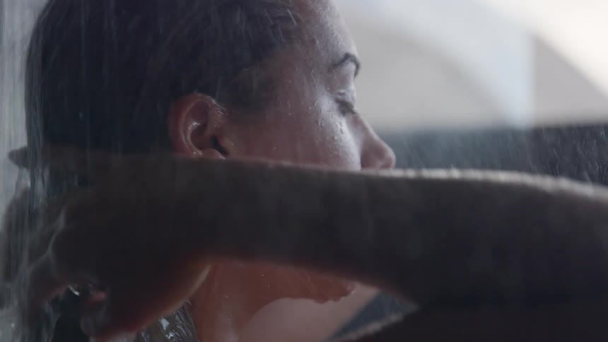 A young woman running her hands through her hair as she takes a shower