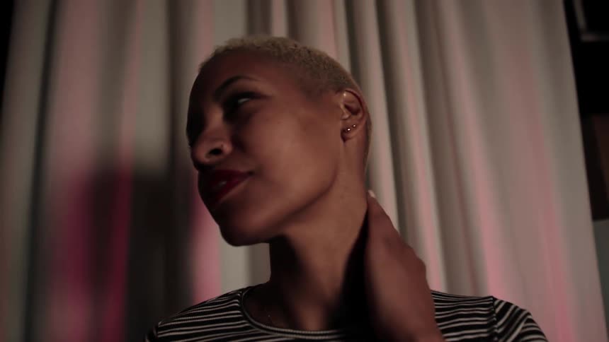 Woman strokes hair and neck next to tall curtain