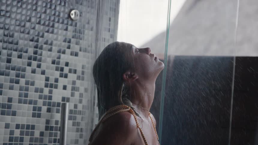 A woman in swimwear taking a shower in room with a large body length window