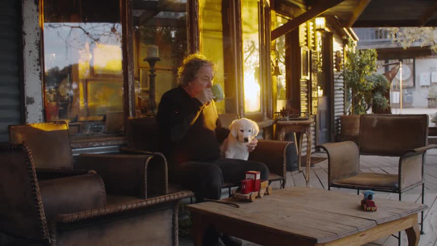 Older man drinking coffee on cafe patio with labrador puppy