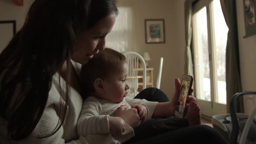 Mother holds her baby while making a video call from her living room