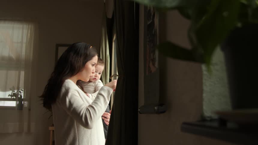 A woman holds her baby as they look out the window