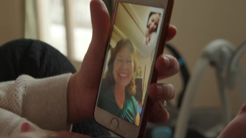 A woman and her baby talk with someone through video chat on a cell phone