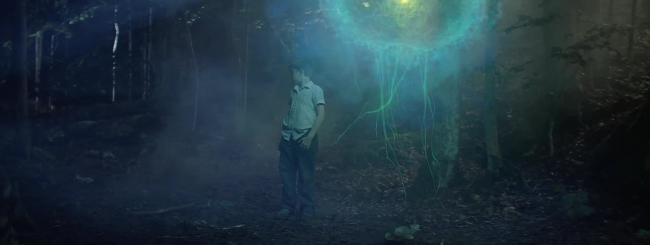 Boy stands in forest at night with alien life form