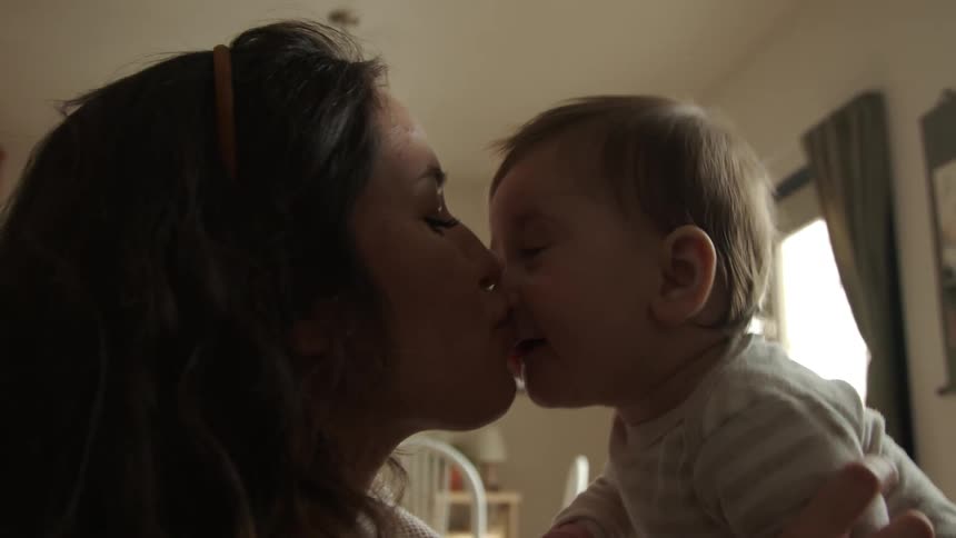 A mom holds her baby up and bounces her as she kisses her faces and makes her laugh