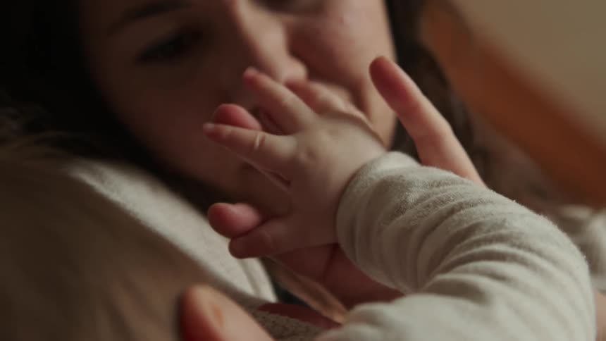 Mother playing with her baby hands while laying on bed
