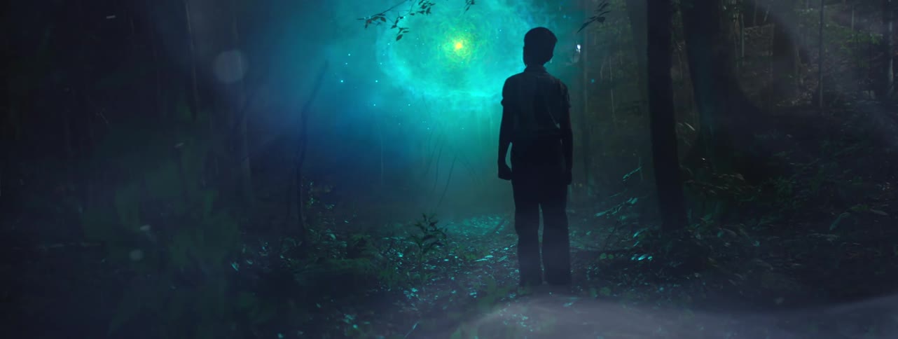 A boy in the forest looking at a blue light