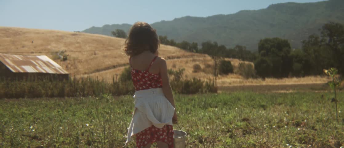 Young girl with a bucket walking through a field on a windy day