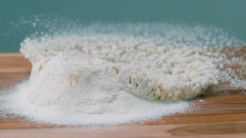 An egg yolk falling into a pile of white powder causing it to splash across a wooden board