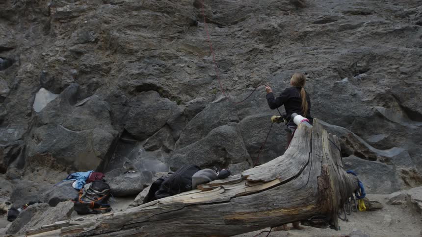 A woman pulls the rope as she watches someone climb up the cliff