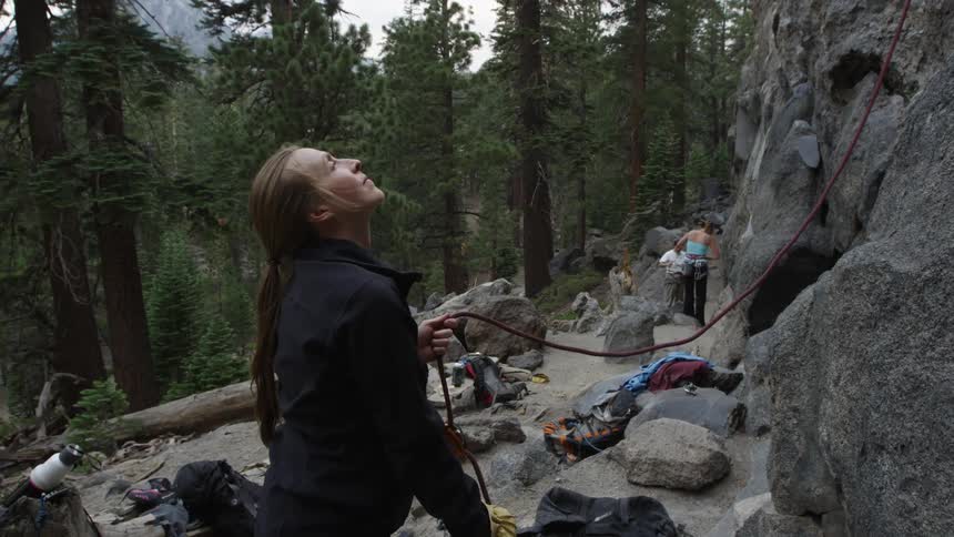 A female rock climber watching looking up a rock face as her rope is prepared