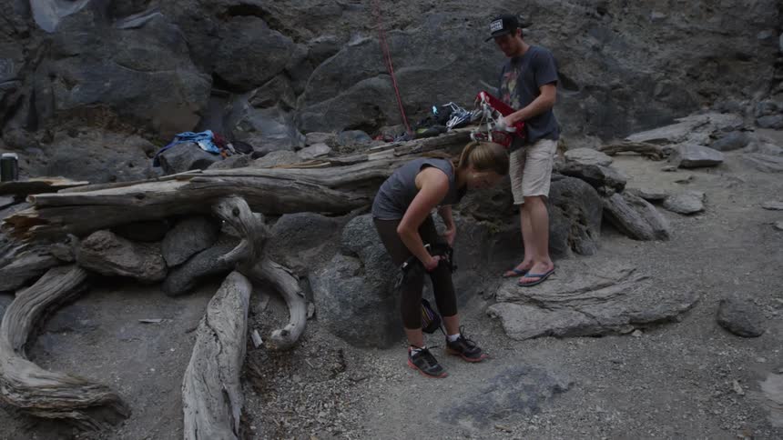 A man and woman put on climbing gear standing next to a large mountain