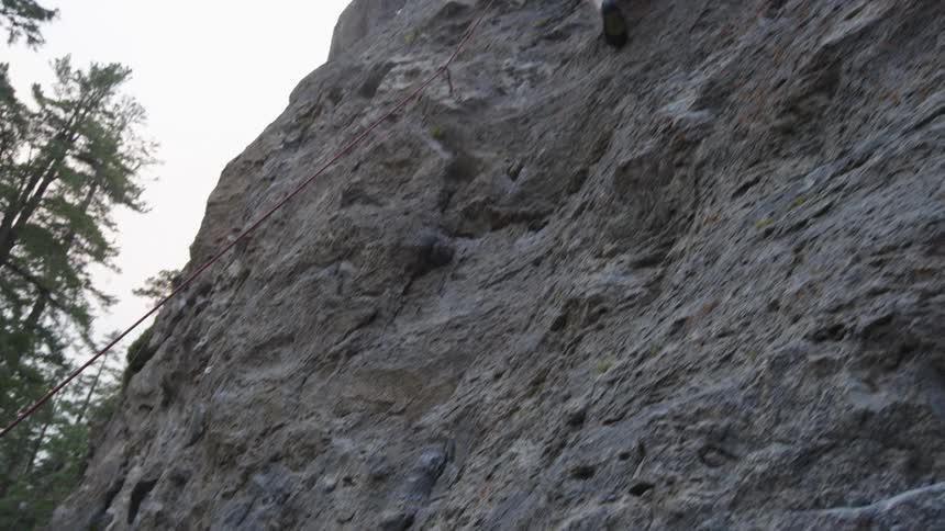 A woman holds the rope as a man climbs up the cliff