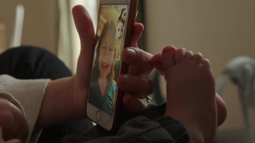 A woman holding a child while video chatting with an older woman on a smartphone