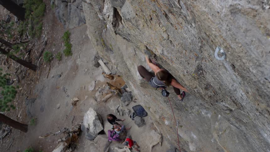 A woman climbs up the side of a mountain as her friends watch from below