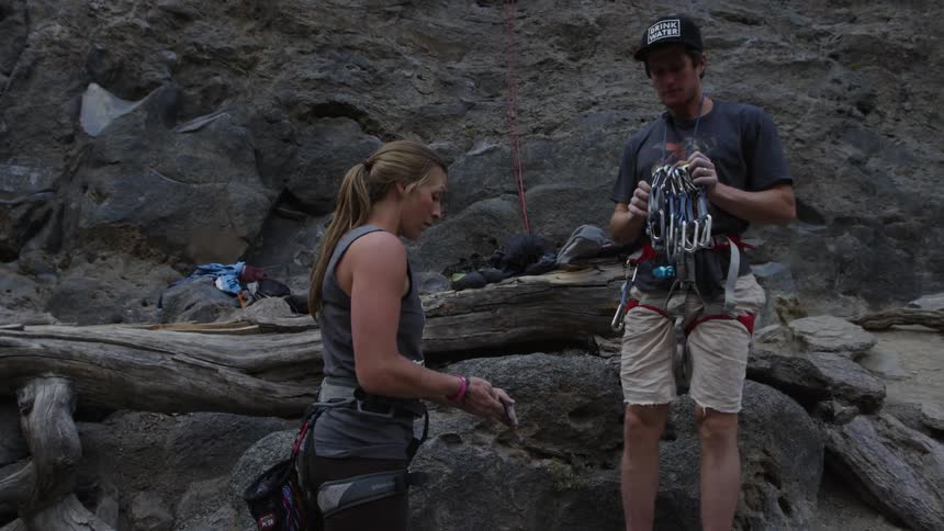 A white man and white woman prepare their climbing gear near the base of a mountain