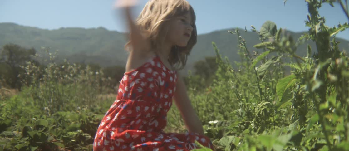 A girl is pulling weeds from a field on a sunny day