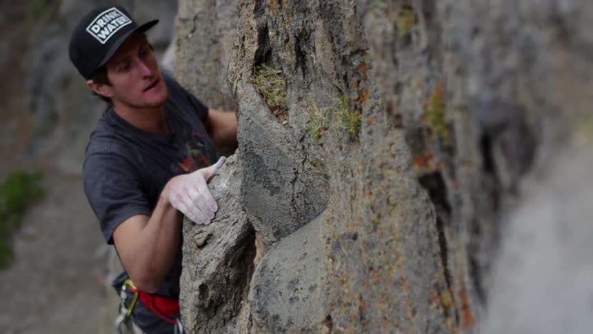 A man scales a rock face in shorts and a short sleeved shirt