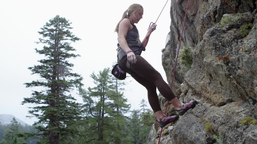 A woman climbs down a mountain side with a climbers rope