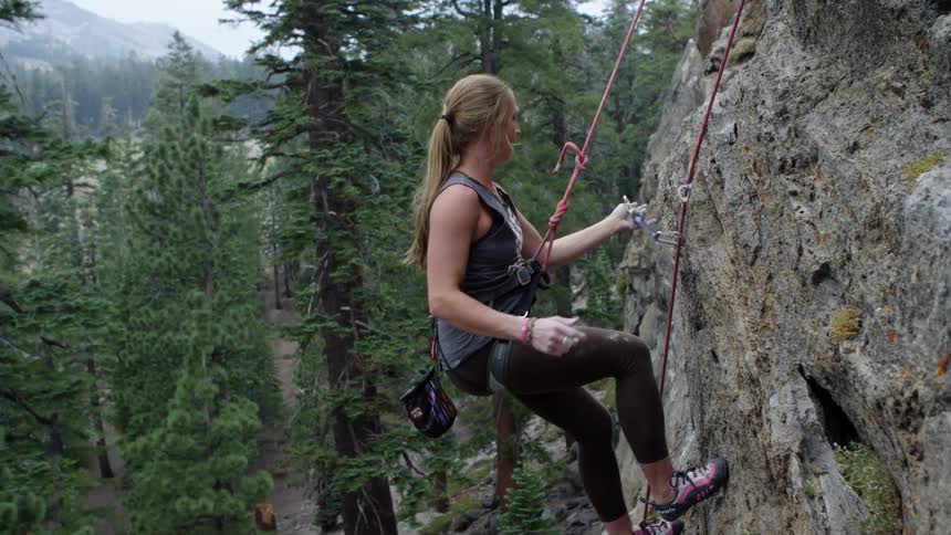 A woman uses clips and a rope while rock climbing a large mountain