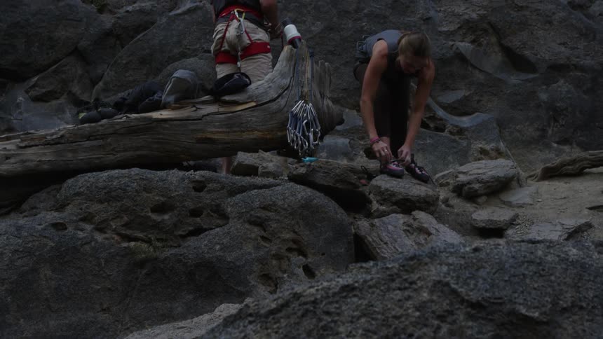 A pair of rock climbers preparing their gear at the base of a rock face before a climb
