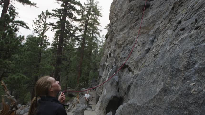 A woman holds a rope for a man rock climbing
