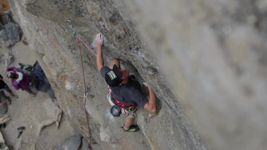 Man does some rock climbing while people wait below