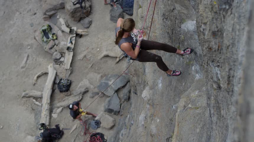 Female rock climber descending cliff face with man below holding rope