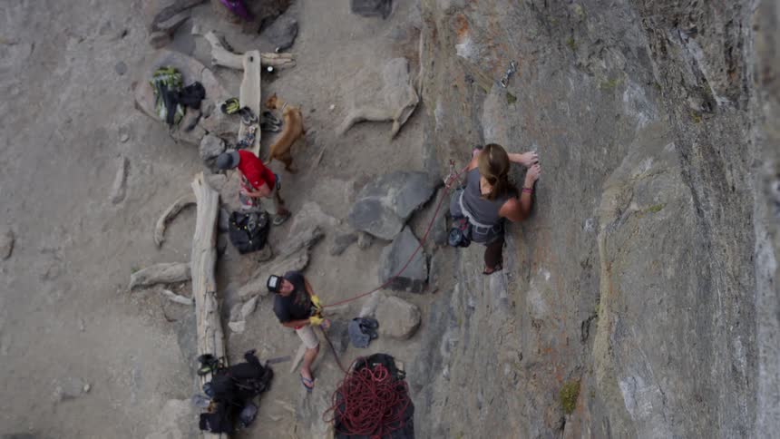 A woman uses a hand hold to pull her self up on a rock climb while a man stands below holding a rope