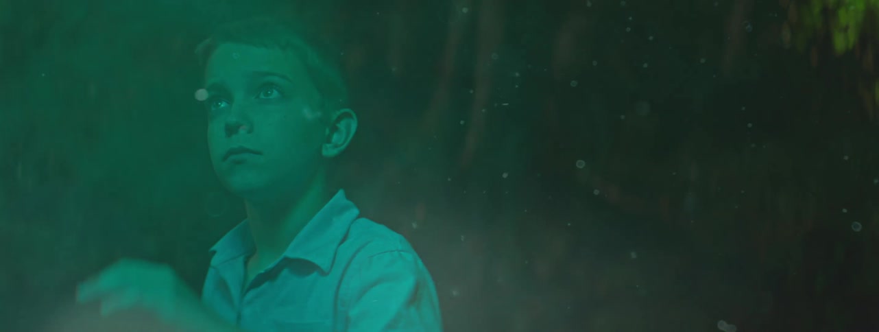 A young white boy retracts his extended arm as smoke moves around him while outdoors