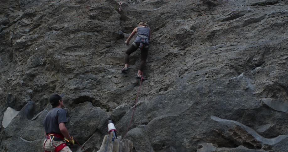 A female rock climber climbs up a rock side