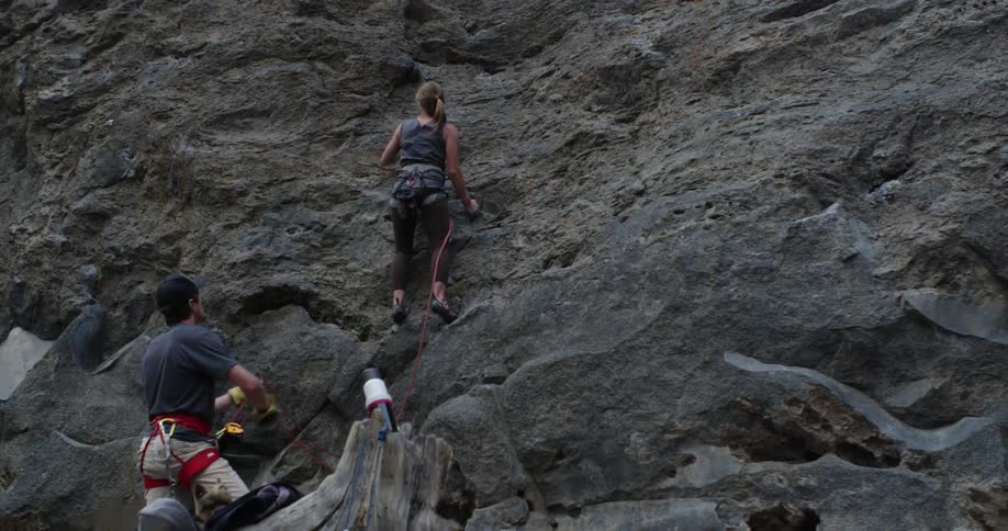 Woman rock climbs while a man watches her from below
