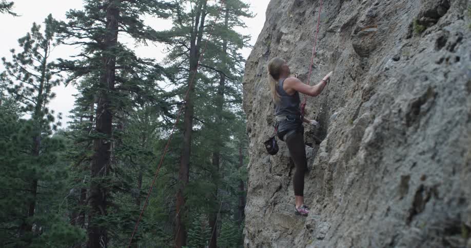 A white female carefully climbs a steep rock face