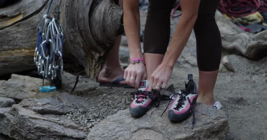 A white female puts on shoes and ties the laces while a white man waits in the background