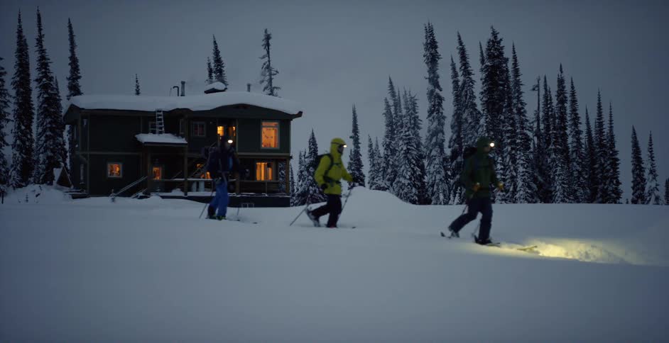 Three people ski touring away from a lodge at night