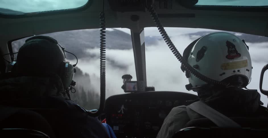Two people flying in a helicopter with mountains in the foreground