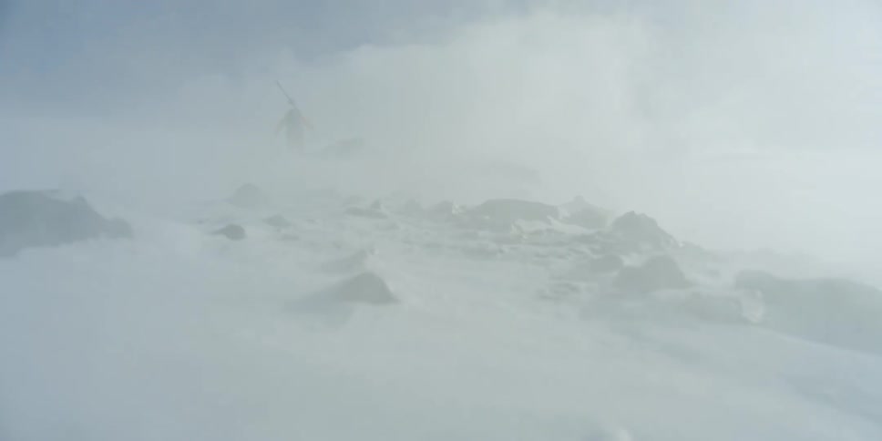 A person walking in a blizzard holding skis