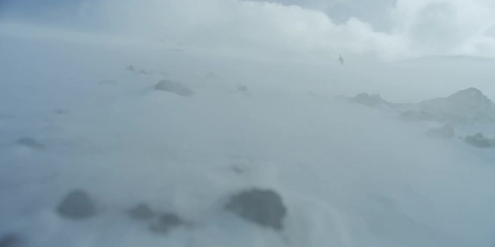 A snow storm is covering the mountains as a person climb beyond