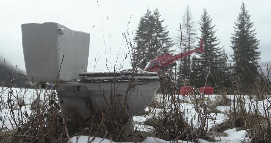 Toilet abandoned in snowy field with a helicopter taking off behind it