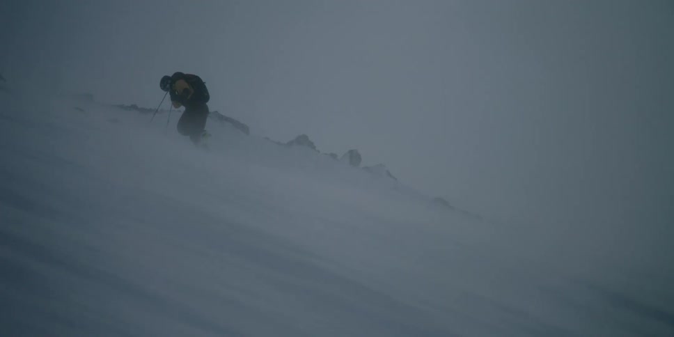 A person climbs a snowy slope through howling wind