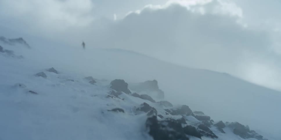 A person at the top of a hill as a snow storm blows over