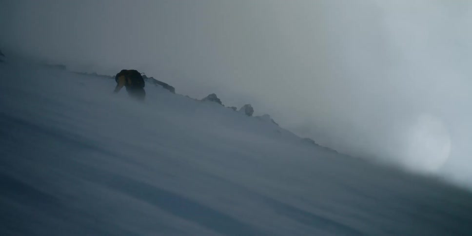 A climber struggling to climb a slope against the snowy wind blowing downhill