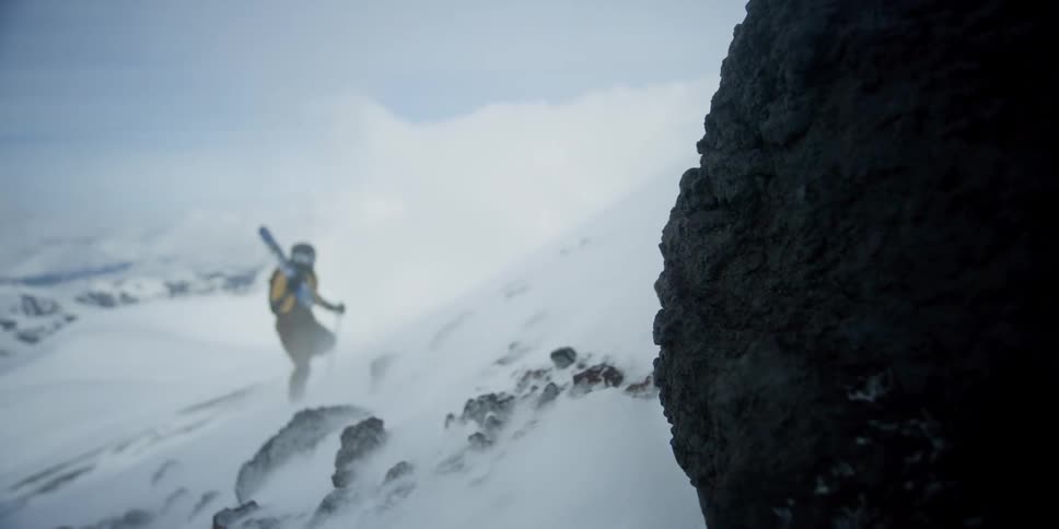 A skier is climbing up the mountain through the windblown snow