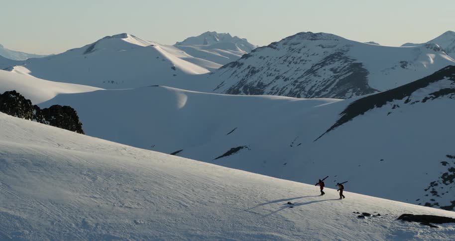 Aerial of two people hiking up a ridge carrying skis