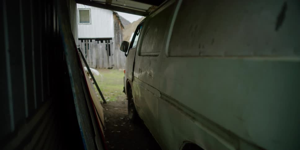 An old van is parked in a shed behind a house