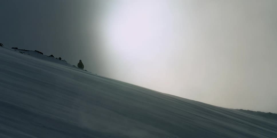 A person stands ona  snowy slope as clouds fly by the sun