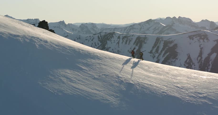 Aerial as two skiers climb a peak with snowy range in the background